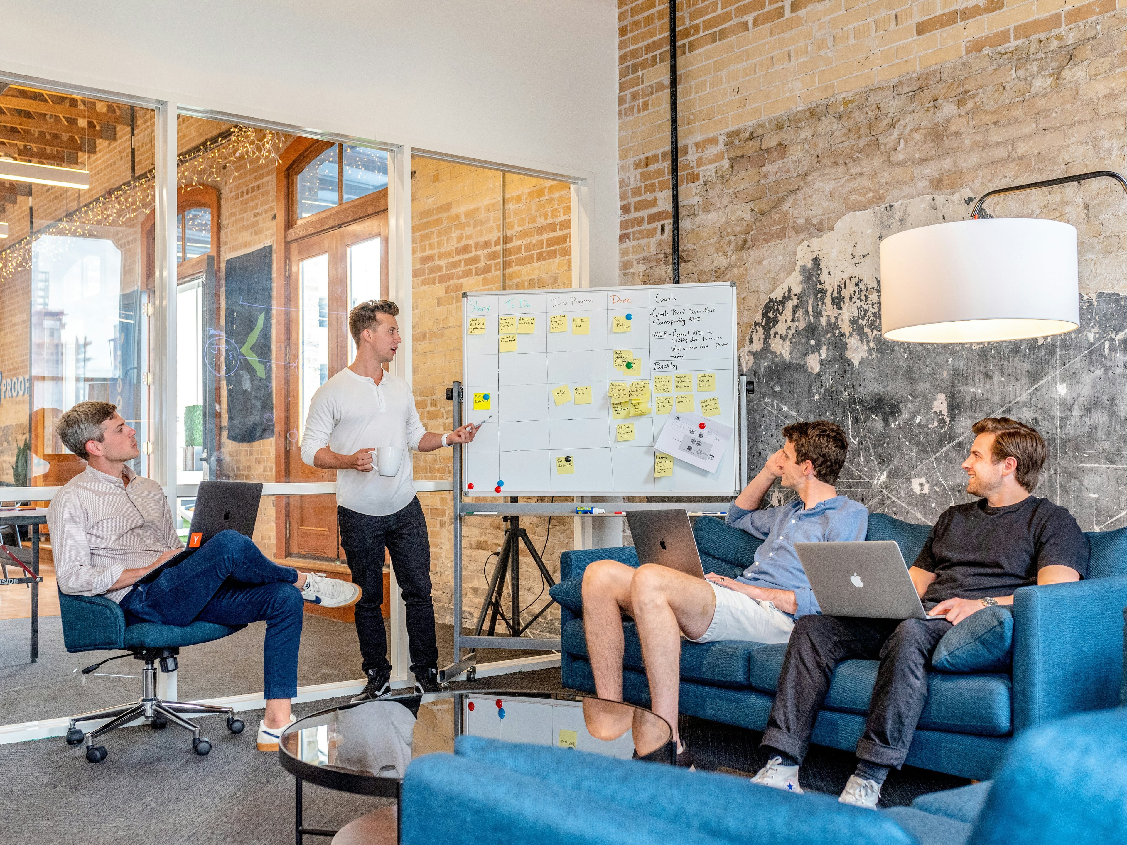 Open-plan studio with exposed brick walls and a wood-beamed ceiling, recruiters working at long desks under industrial lighting.