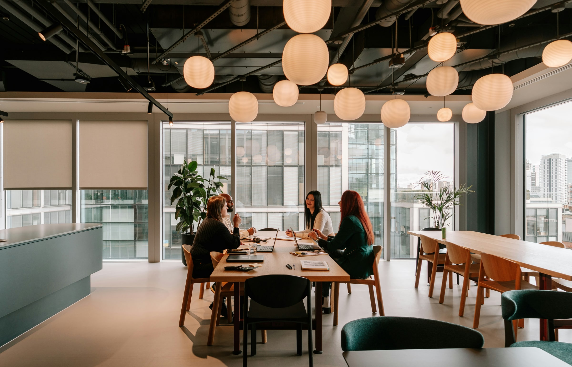 Small team in conversation around a meeting table in a modern co-working office, warm pendant lights overhead.